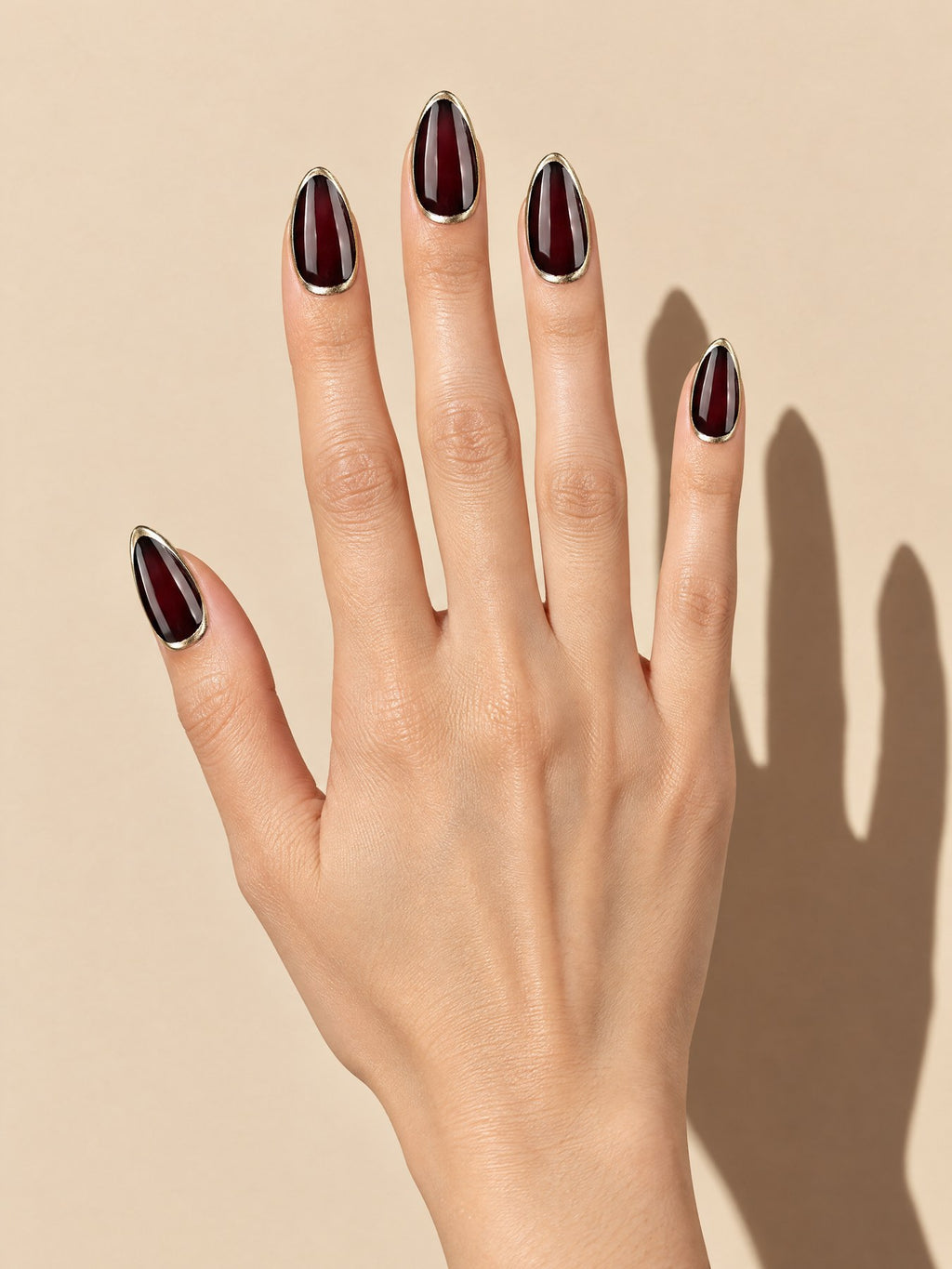 Black Cherry Gold Rim Almond Press-On Nails on a hand