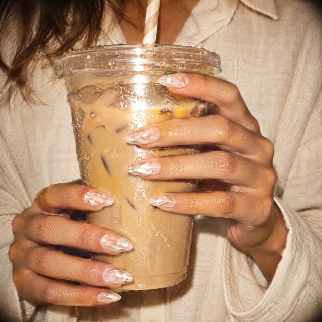 Hand with gold swirl chrome press-on nails holding an iced latte