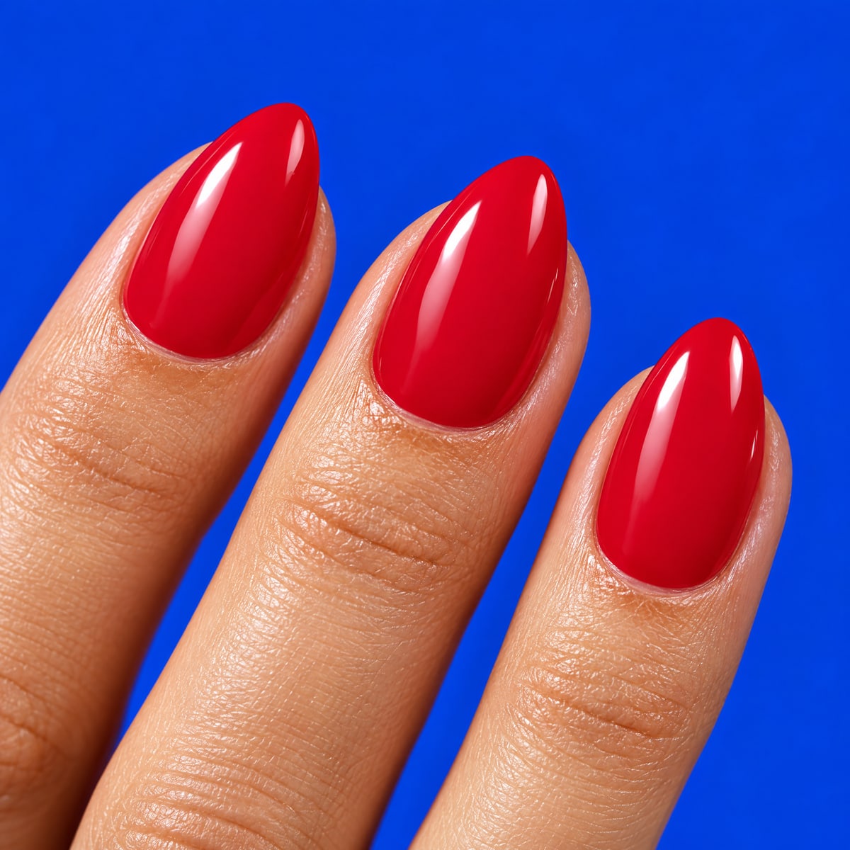 Macro texture tile: solid glossy cherry red almond nails on cobalt blue